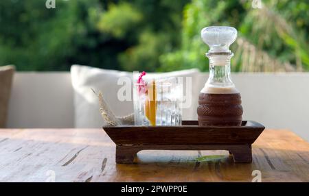 Beginnen Sie mit Mocktail-Getränken, und fügen Sie die Mischung mit Himbeere, Jasmin und Thaitea hinzu. Ein Glas Eis, Orangenschale und Wildblumen neben einem hohen Glas Stockfoto