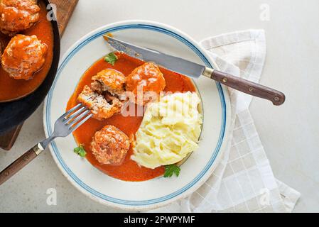 Gebratene Fleischbällchen, geschmort in Tomatensauce, serviert mit Kartoffelpüree auf einem weißen Tisch. Ich esse mit Rind gebratene Fleischbällchen in Tomatensoße. Stockfoto