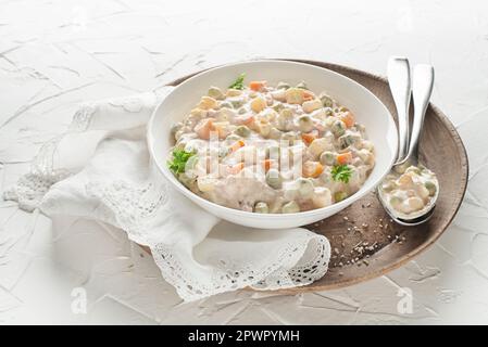 Schüssel mit russischem Salat olivier französischer Salat mit Gemüse und Ei mit Mayonnaise auf weißem Tisch Stockfoto