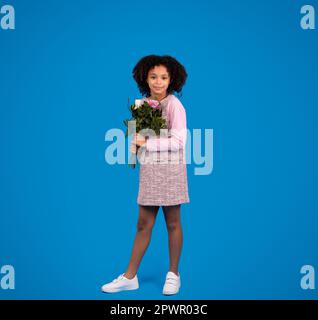 Lächelndes afroamerikanisches kleines Mädchen mit Blumenstrauß isoliert auf blauem Hintergrund Stockfoto