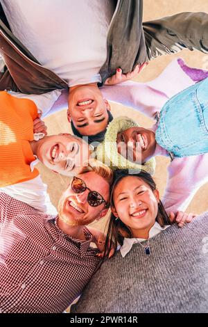 Vertikale Ansicht eines multirassenfreundlichen jungen Freundes, die Spaß haben und in die Kamera schauen. Unteres Porträt einer Gruppe von multiethnischen fröhlichen Menschen, die auf einem Kreis stehen, der sich verbindet. Hochwertiges Foto Stockfoto
