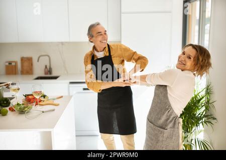 Romantisches Seniorenpaar, das tanzt, zusammen Spaß bei Musik im Küchenbereich hat, Kopierraum Stockfoto