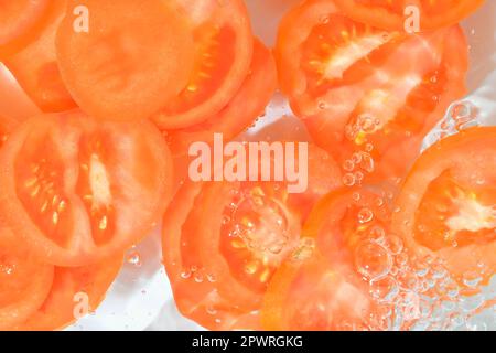 Nahaufnahme frischer Tomatenscheiben auf weißem Hintergrund. Tomatenscheiben in sprudelndem Wasser auf weißem Hintergrund, Nahaufnahme. Horizontales Bild. Stockfoto