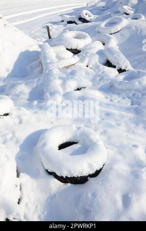 Gebrauchte und entsorgte Autoreifen liegen am Straßenrand und sind mit einer dicken Schneeschicht bedeckt Stockfoto