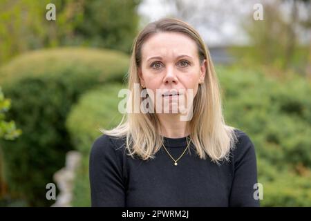 Eine wunderschöne blonde Frau in den 40s Jahren, die ein schwarzes Hemd und eine Halskette trägt, lächelt und macht einen erschöpften oder enttäuschten Gesichtsausdruck Stockfoto