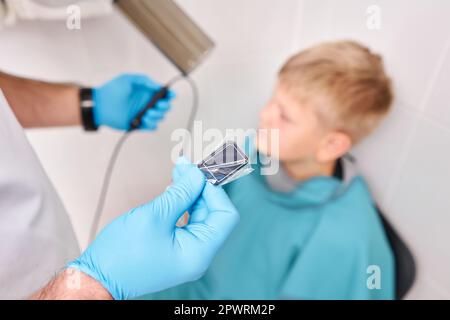 Arzt zeigt Röntgengerät mit elektronischem Sensor beim Kind. Der Zahnarzt bereitet den Jungen auf das Zahnröntgenbild in der Zahnklinik vor. Stockfoto