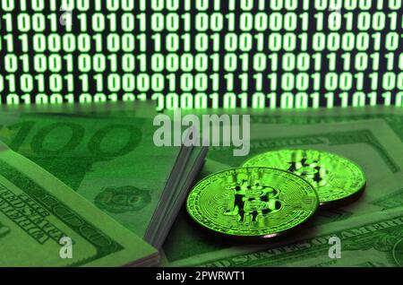 Zwei bitcoins liegt auf einem Stapel von dollarnoten auf dem Hintergrund eines Monitors mit der Darstellung eines binären Code der helle grüne Nullen und 1 Einheiten auf einem Schwarz Zurück Stockfoto