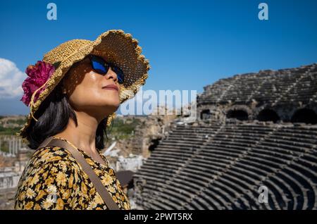 Eine vietnamesische Asiatin mit Hut und Sonnenbrille besucht das große und gut erhaltene römische Amphitheater in Side in der Provinz Antalya, Tur Stockfoto