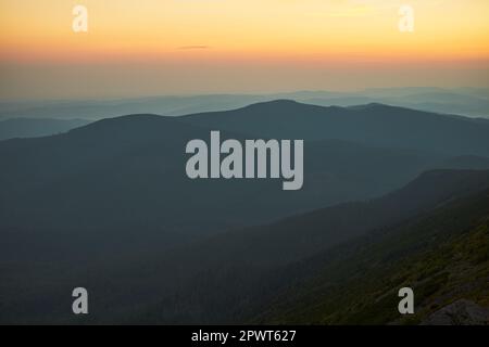 Sonnenaufgang in den Bergen. Natürliche Berglandschaft mit beleuchteten nebligen Gipfeln, nebligen Hängen und Tälern, blauer Himmel mit orangefarbenem gelbem Sonnenlicht. Unglaublich Stockfoto
