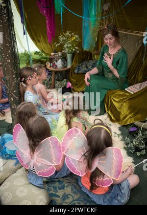 Mädchen mit Feenflügeln, die einem Vortrag einer in Grün gekleideten Dame zuhören, die die Feenkönigin und eine Feenmesse repräsentiert Stockfoto