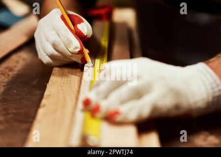 Nur eine kleine Markierung. Nahaufnahme eines unbekannten Zimmermanns, der nachts Messungen an einem Stück Holz in einer Werkstatt vornimmt Stockfoto