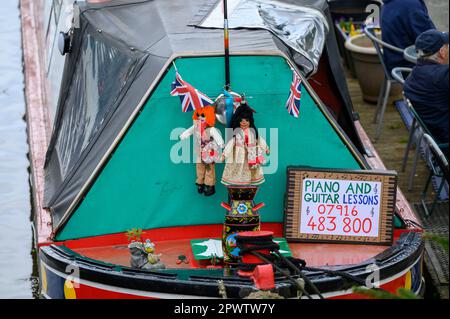 Neben zwei Puppen am Bug eines festgemachten Schmalbootes, das Gitarre- und Klavierunterricht anbietet, steht ein Schild. Stockfoto