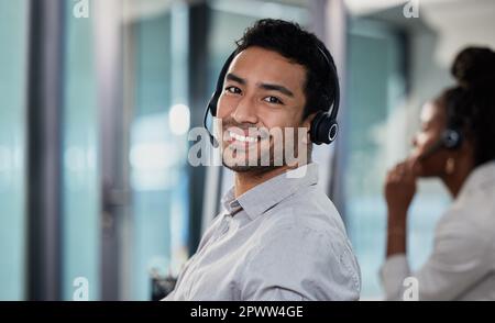 Ich bin bereit, Kunden noch heute zu helfen. Ein attraktiver junger Kundendienstmitarbeiter, der im Büro sitzt und ein Headset trägt Stockfoto