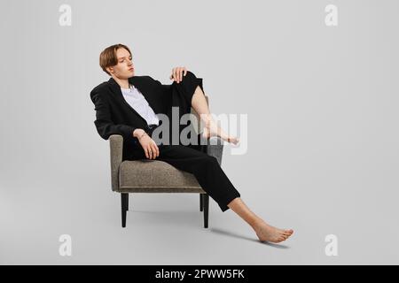 Junger Barfußmann im schwarzen Anzug, der im Sessel im Studio sitzt Stockfoto