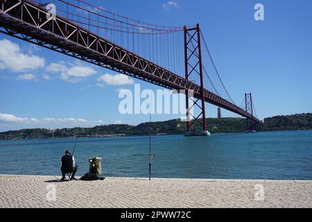 Einzelangler am Ufer des Flusses Tagus unter der berühmten Hängebrücke 25 de Abril Bridge in Lissabon, Portugal, Europa Stockfoto