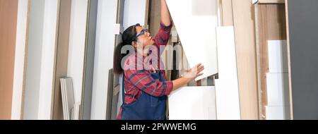 Eine Frau mittleren Alters, die Sperrholz aus einem Lagerfach zieht. Asiatischer Zimmermann arbeitet in einer Möbelfabrik. Stockfoto