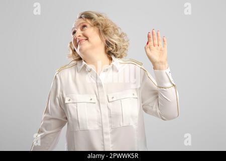 Eine ältere Frau winkt ungläubig über grauen Hintergrund mit der Hand Stockfoto