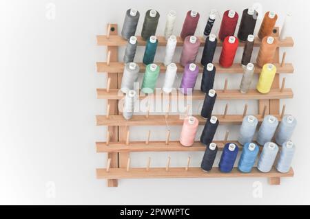 Eine Sammlung von mehrfarbigen Nähfäden, die auf einem hölzernen, wandmontierten Gewinderahmen mit Schieber auf weißem Hintergrund mit Kopierbereich dargestellt werden Stockfoto