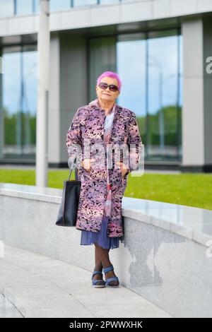 Porträt einer Seniorin mit rosa Haaren und Kaschmirmantel, die spazieren geht Stockfoto