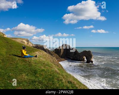 Frau saß an einem sonnigen Tag im März auf einer Klippe über Durdle Tür und Strand, Dorset, Großbritannien Stockfoto