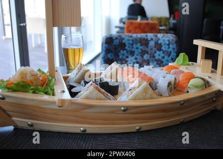 Sushi und Brötchen in der Boat Bar aus recyceltem Holz mit einem Glas Bier in einem Fischrestaurant Stockfoto