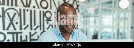 Lächelnder afrikanischer Geschäftsmann, der in einem modernen Coworking sitzt und einen Laptop arbeitet Stockfoto