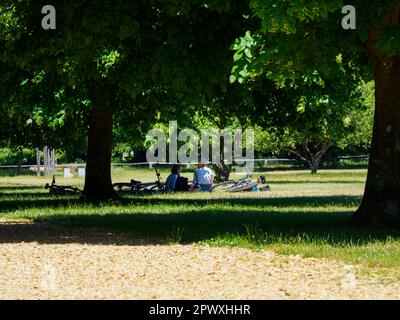 Familie mit Fahrrädern im Schatten eines Baumes im Royal Victoria Country Park, Netley, Hampshire. Stockfoto