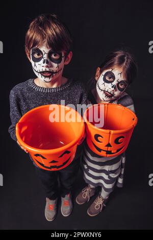 Zwei Kinder mit Totenkopf Make-up halten Kürbis Eimer an Halloween. Stockfoto