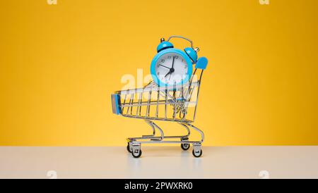Runder Wecker in einem kleinen Einkaufswagen auf gelbem Hintergrund Stockfoto