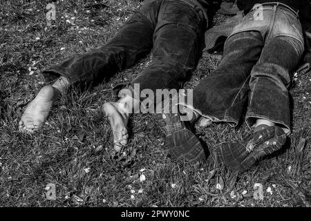 Füße eines jungen Paares, Mann barfuß, Mädchen mit Schuhen. Er lag im Frühling auf dem Gras. Konzeptbeziehung, Entspannung, Gesellschaft, Liebe. Schwarz und Weiß. Stockfoto