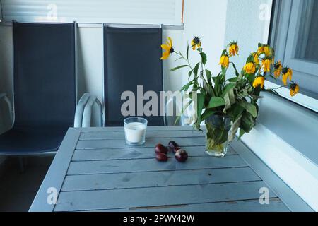 Pflanzen und Blumen der Jerusalem-Artischocke in einer Vase. Kastanienfrüchte auf dem Tisch. Tisch und Stühle auf dem Balkon oder der Terrasse. Ende der Saison in der Hure Stockfoto