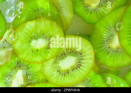 Nahaufnahme von Kiwis in Flüssigkeit mit Blasen. Scheiben von grünen, reifen Kiwis im Wasser. Nahaufnahme frischer Scheiben grüner Kiwis auf weißem Hintergrund. Stockfoto