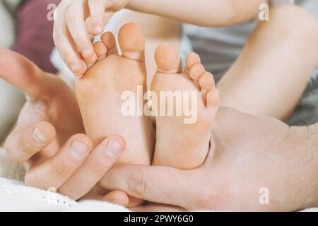 Kinderfüße in den Händen des Vaters. Papa kitzelt die Füße des Kindes. Baby zählt Zehen Stockfoto