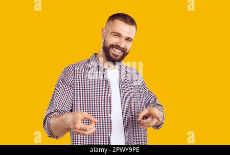 Ein fröhlicher Mann lächelt und zeigt mit zwei Zeigefinger auf einen orangefarbenen Hintergrund. Stockfoto