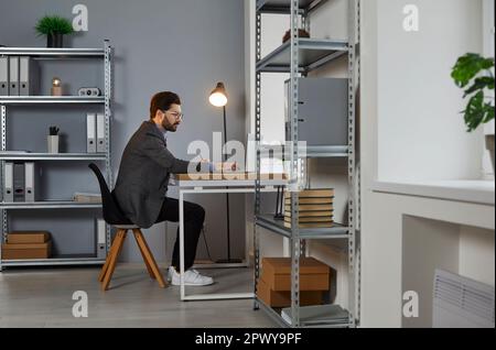 Junger Geschäftsmann, der am Schreibtisch an seinem Arbeitsplatz im Büro arbeitet Stockfoto