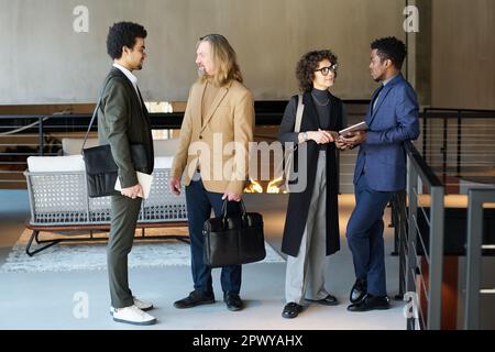 Interkulturelle Kollegen in formeller Kleidung teilen aktuelle Neuigkeiten auf der Börse mit oder besprechen organisatorische Momente vor der Geschäftskonferenz Stockfoto