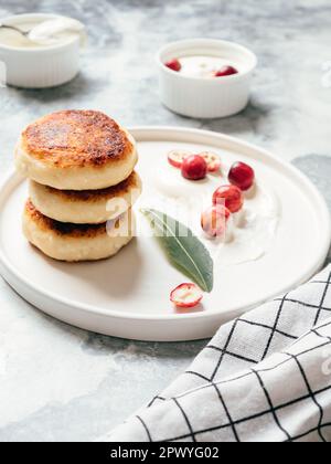 Hüttenkäse-Pfannkuchen auf einem Tisch mit Sauerrahm und Beeren. Leckere und gesunde Käsekuchen mit Cranberry zum Frühstück. Leckeres Dessert Stockfoto