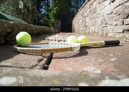 Drei Tennisbälle und ein alter Schläger auf dem Weg Stockfoto