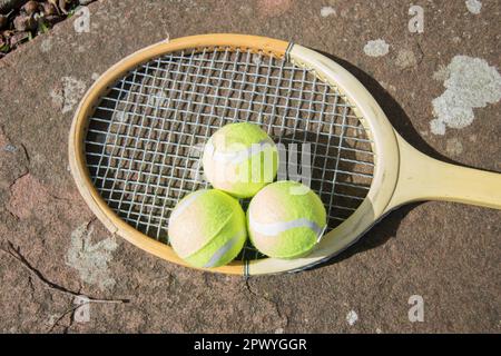 Drei Tennisbälle und ein alter Schläger auf dem Weg Stockfoto