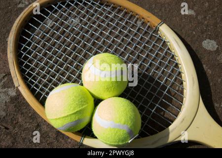 Drei Tennisbälle und ein alter Schläger auf dem Weg Stockfoto