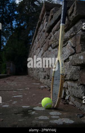 Drei Tennisbälle und ein alter Schläger auf dem Weg Stockfoto