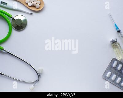 Medizin-Wohnung. Gesund-und Krankheitskonzept. Pillen in Holzlöffel, Thermometer, Stethoskop und Spritze auf weißem Hintergrund mit Kopierbereich. Suppl Stockfoto