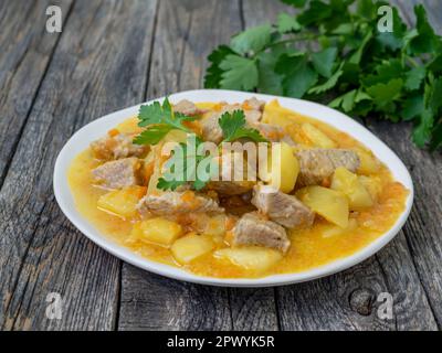 Rumänische Küche: Frisches hausgemachtes Fleisch und Kartoffeln mit Petersilie. Eintopf mit Schweinefleisch und Gemüse auf Holzhintergrund. Leckeres und nahrhaftes Mittagessen. Stockfoto