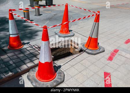 Die Reparatur von Straßenkühllöchern. Rote Reparaturkegel, die die Straße umzäunen Stockfoto