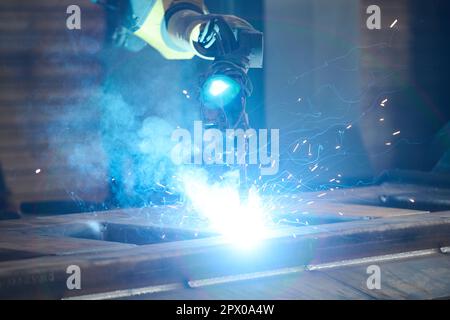 Lichtbogenschweißverfahren, das von großen Roboteranlagen in einer großen Werkstatt einer zeitgenössischen Maschinenfabrik erzeugt wird Stockfoto