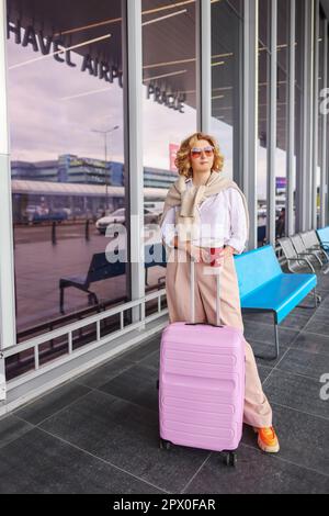 Ungezwungenes junges Mädchen mit pinkfarbenen Koffern, die in der Flughafenterminalhalle warten und Kaffee trinken. Konzentrieren Sie sich auf die Frau. Stockfoto