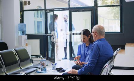 Seniorin-Kontrolle mit Glukometer-Instrument, Krankenschwester misst Glukosespiegel mit Insulin-Test. Assistentin zur Blutprobenkontrolle bei Diabetikern in der Krankenhausrezeption. Stockfoto