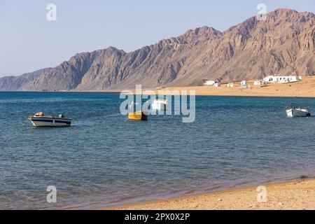 Blick auf das Rote Meer und Boote im Hafen, Dahab, Ägypten. Dahad ist ein ehemaliges Beduinendorf, umgeben von Bergen, heute eines der wertvollsten di Stockfoto