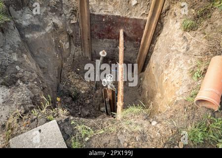 Ein Loch wurde gegraben, um das Rohr zu reparieren und den Hahn zu wechseln. Abwassergraben mit Rohren. Reparatur unterirdischer Kommunikation. Abwasser- und Wasserleitung unter dem g Stockfoto