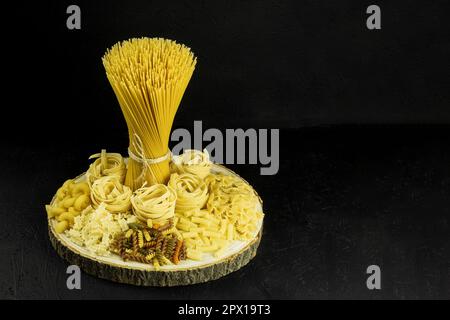 Eine Auswahl an Pasta und Spaghetti auf dunklem Hintergrund. Rohe Pasta zum Kochen italienischer Küche auf einem Holztisch auf dunklem Hintergrund. Speicherplatz kopieren Stockfoto